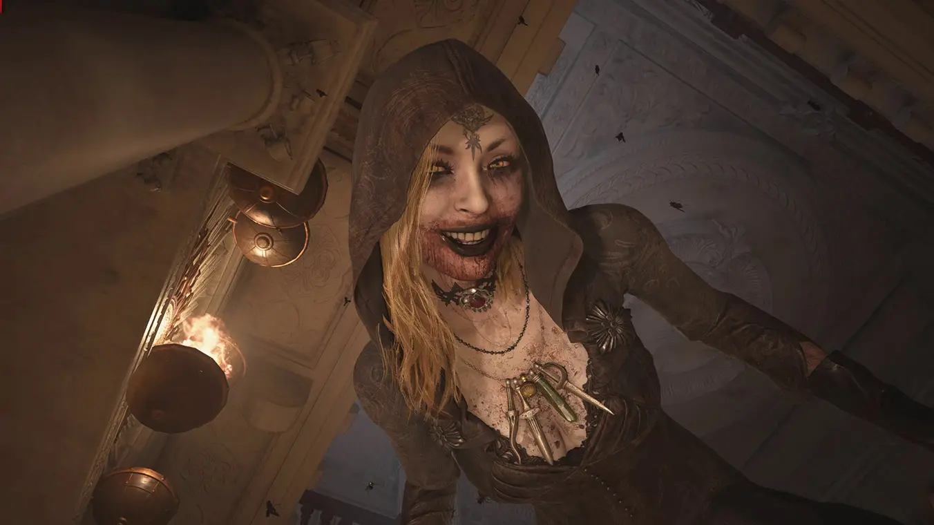 A low-angle, close-up screenshot of one of Lady Dimitrescu's daughters peering down menacingly. She wears a dark, tattered hood, has blood smeared across her wide smile, and exposes pale skin marked with a tattoo on her forehead.